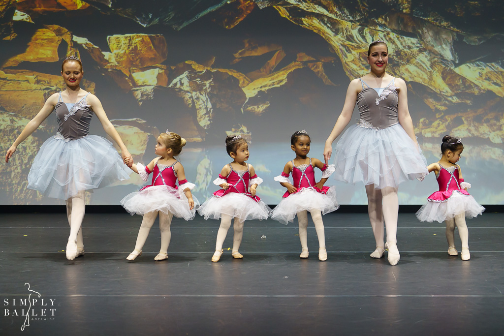 Toddler ballet dancers onstage with older girls helping