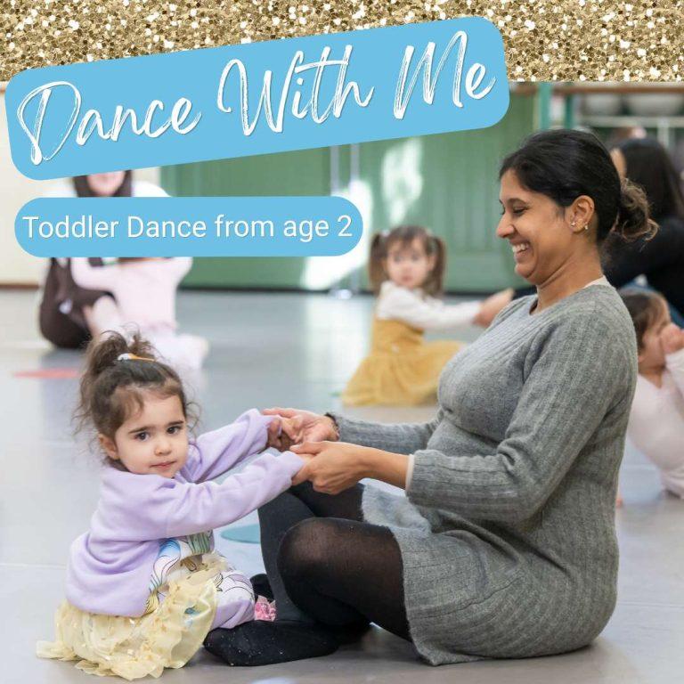 Mother sitting on the floor with their toddler in a dance class smiling and holding hands